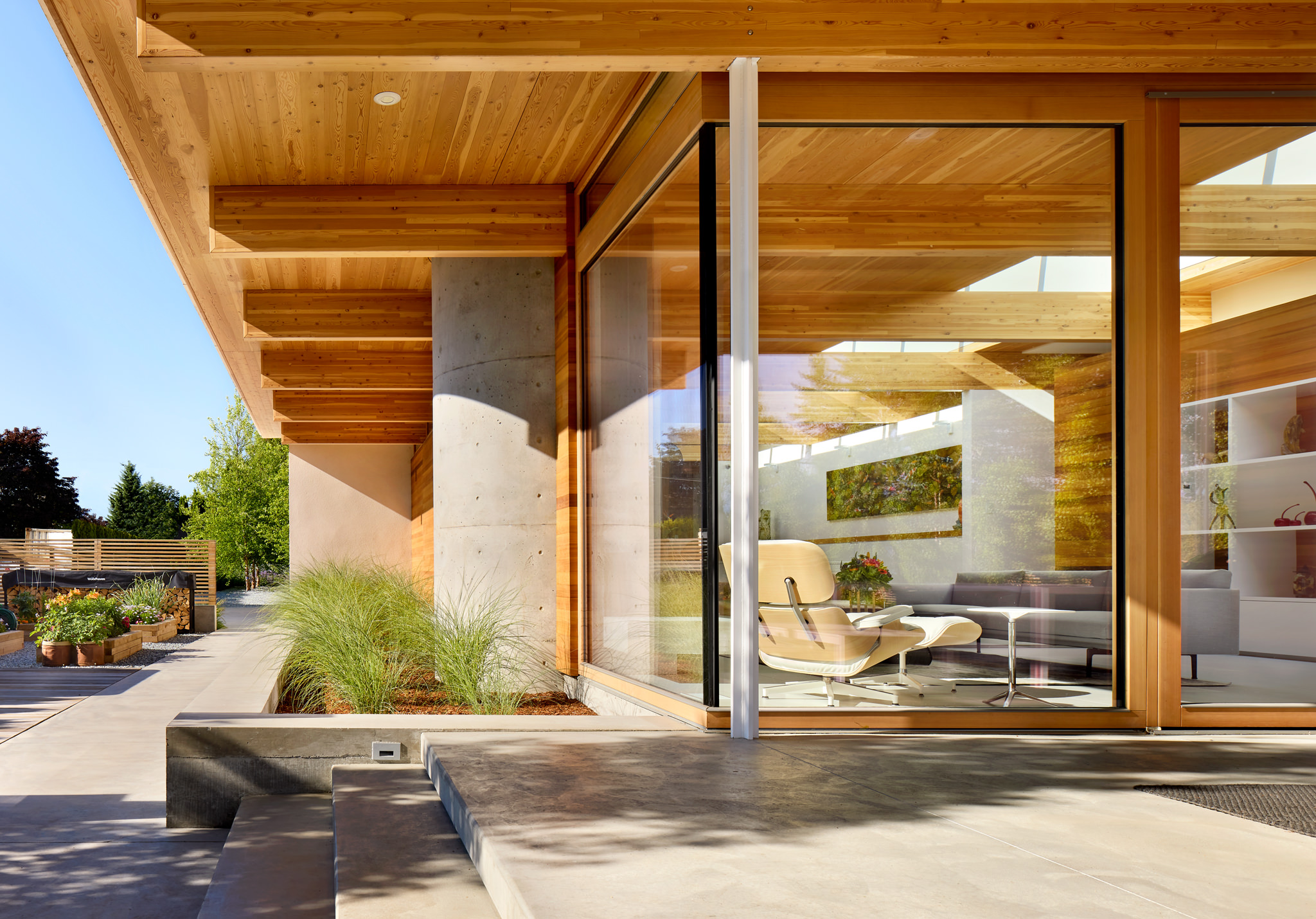 View to interior though large glass doors of modern wood house with Eames chair inside