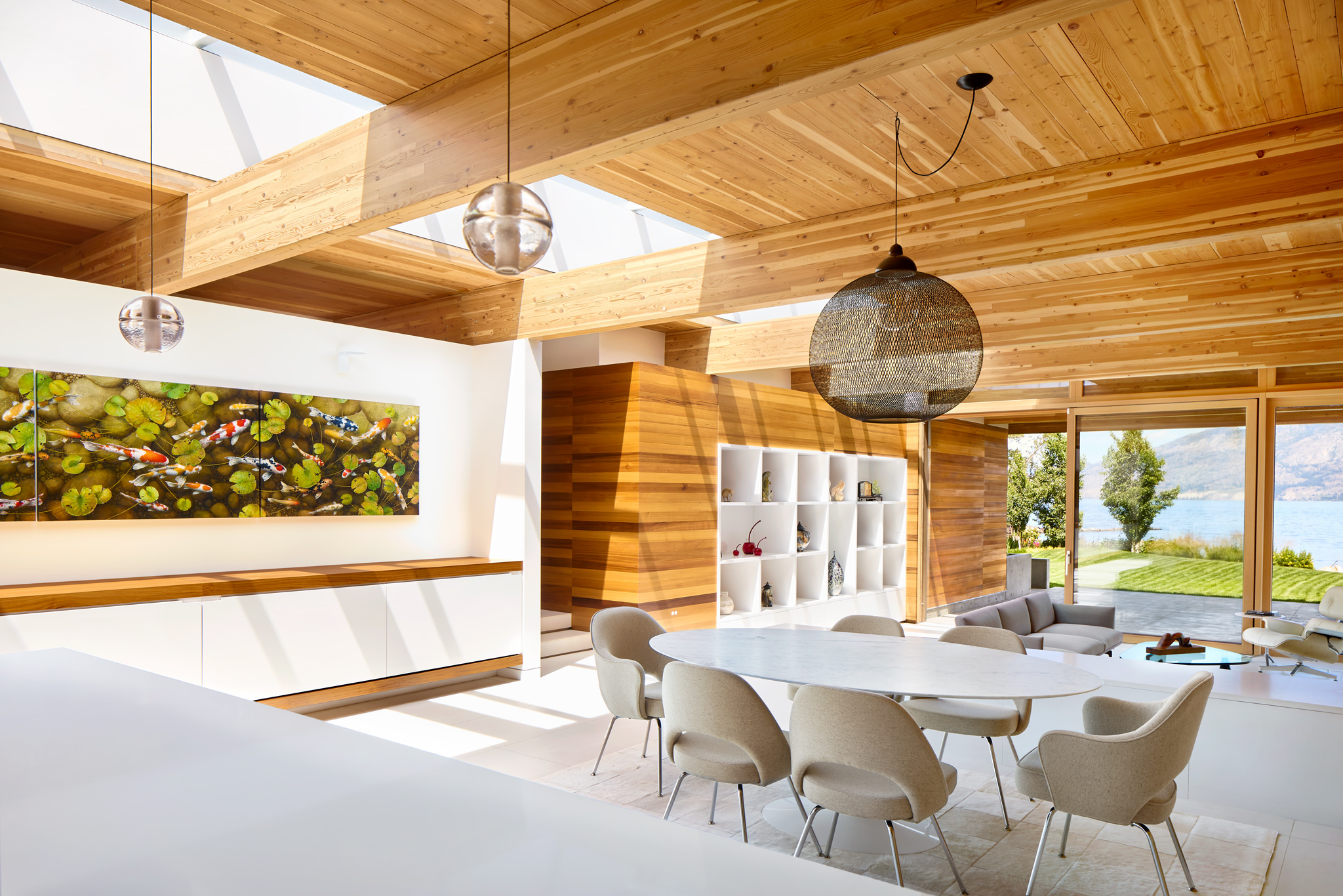 Interior view of bright modern home with wood materials and art looking out to lawn and lake