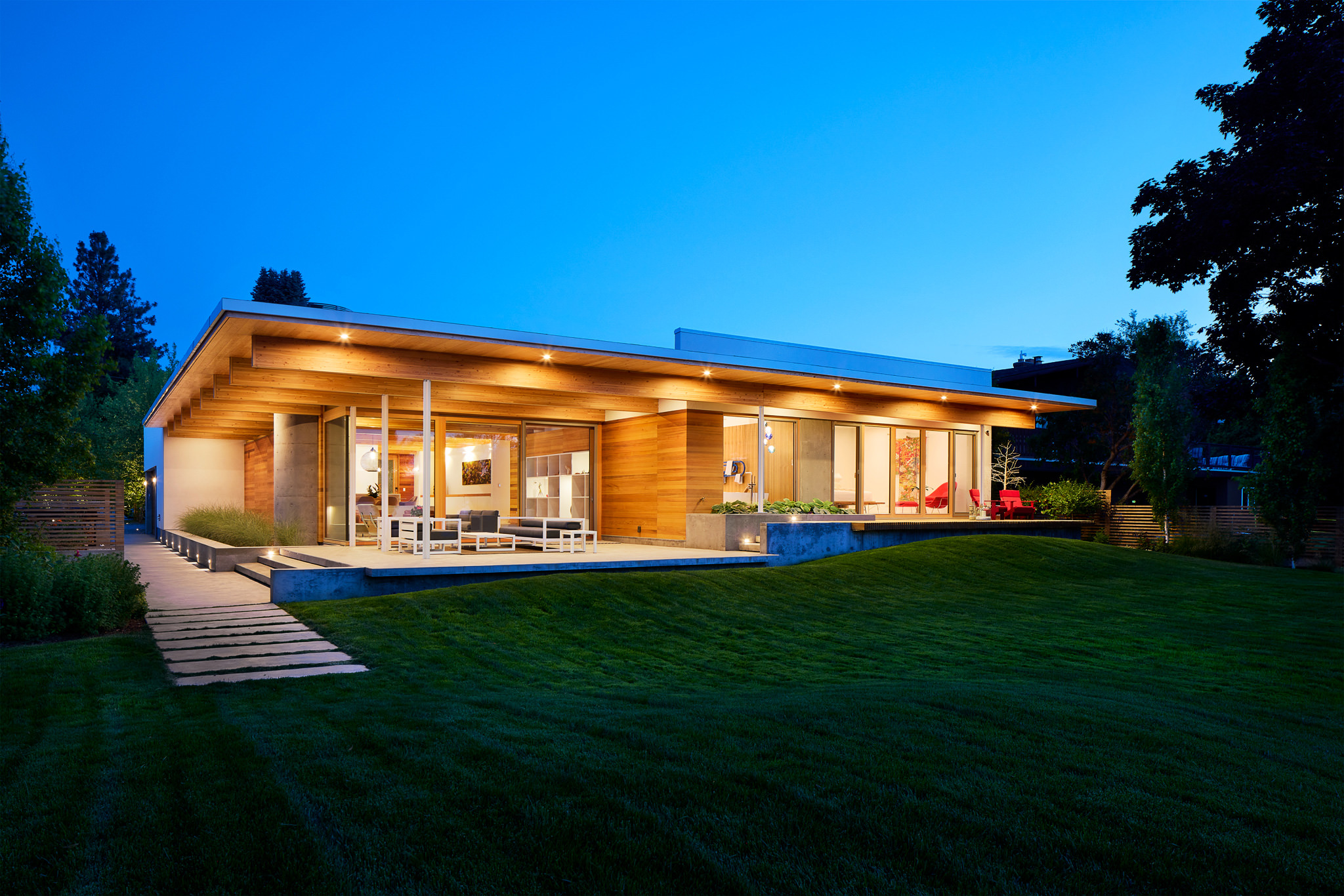 Dusk view of modern residence featuring wood finishes and lawn foreground