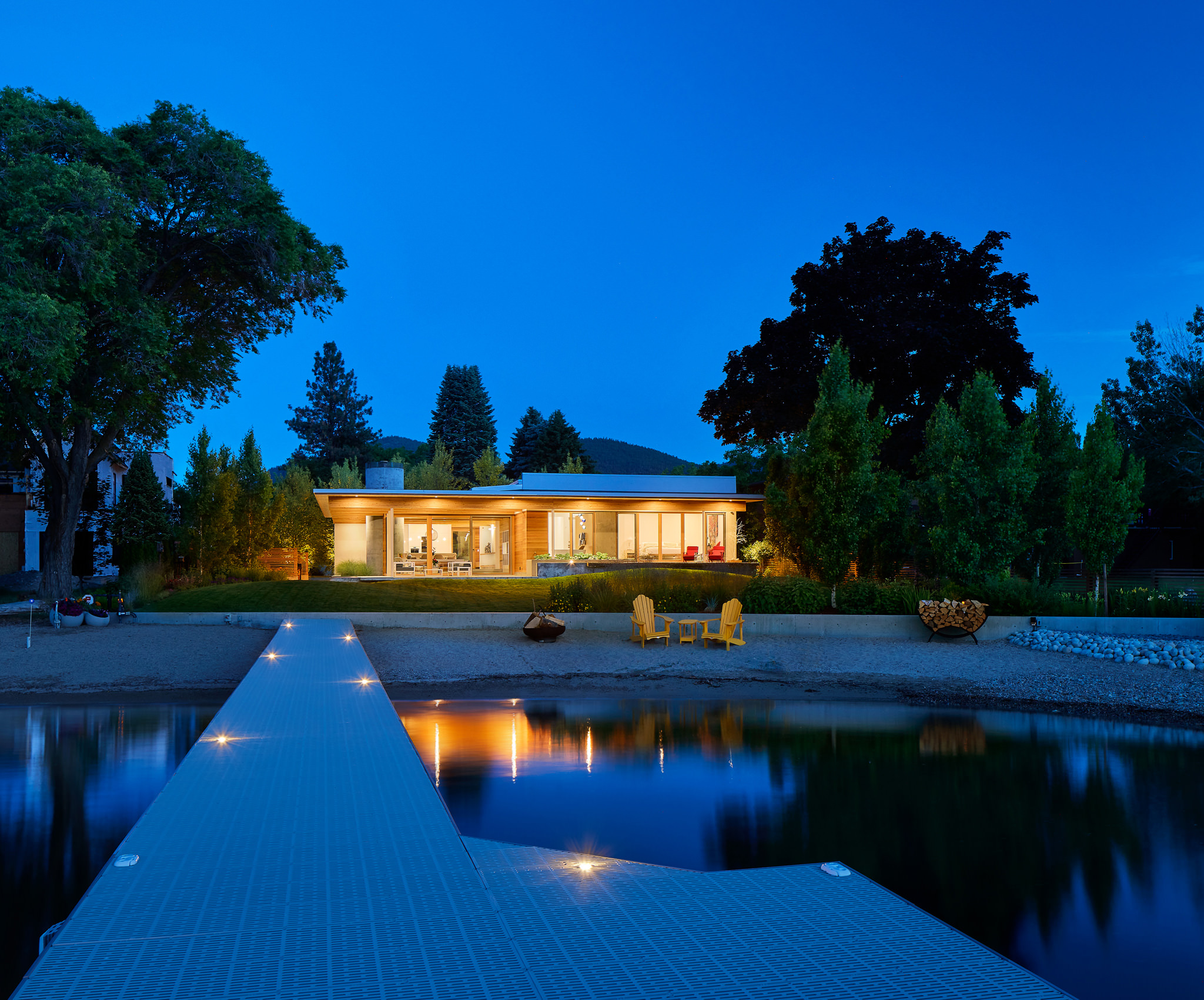 Dusk view from dock of modern residence featuring wood finishes lawn foreground surrounding trees and mountains